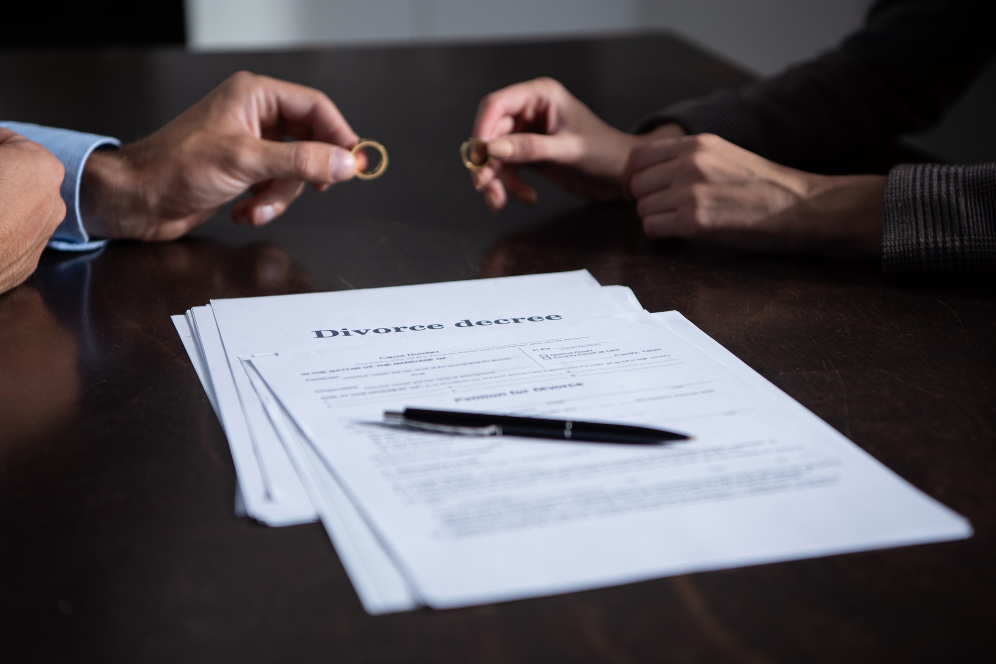partial view of couple at table with divorce documents holding rings